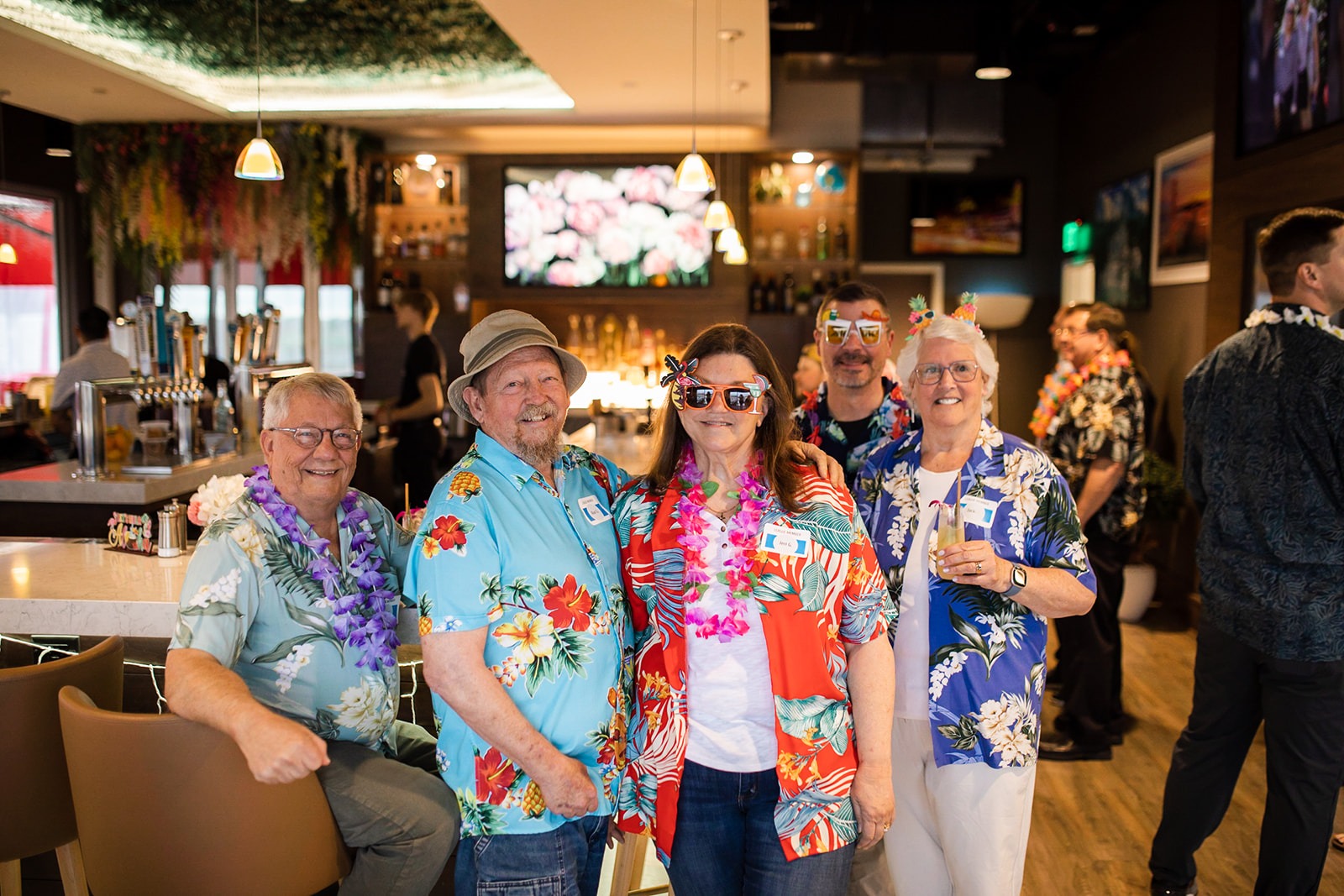 group of people smiling in a restaurant wearing hawaiian gear