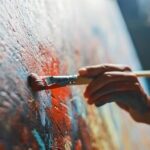 Female Artist Works on Abstract Oil Painting, Moving Paint Brush Energetically She Creates Modern Masterpiece. Dark Creative Studio where Large Canvas Stands on Easel Illuminated. Low Angle Close-up
